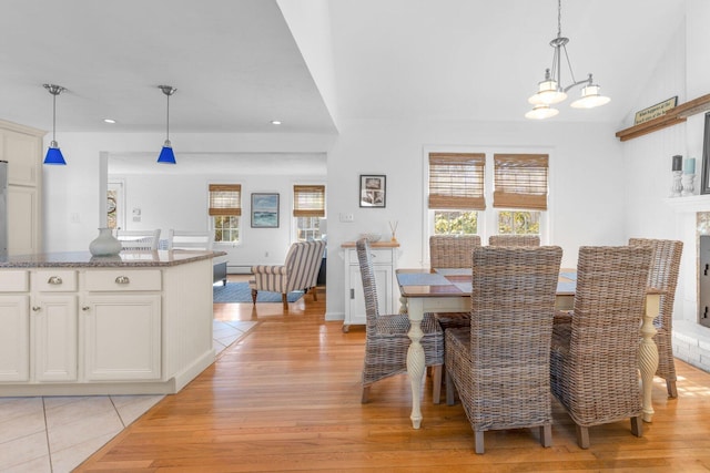 dining space featuring lofted ceiling, light wood-style flooring, recessed lighting, a fireplace, and an inviting chandelier