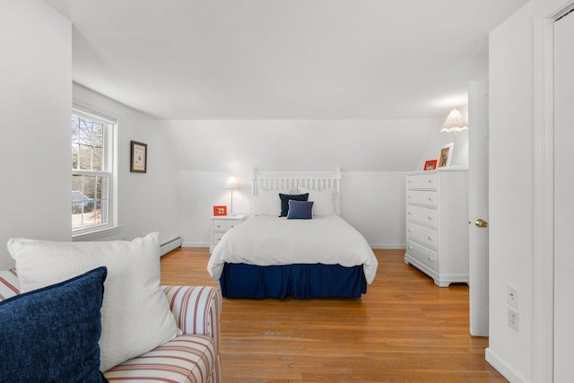 bedroom featuring lofted ceiling, light wood finished floors, a baseboard radiator, and baseboards