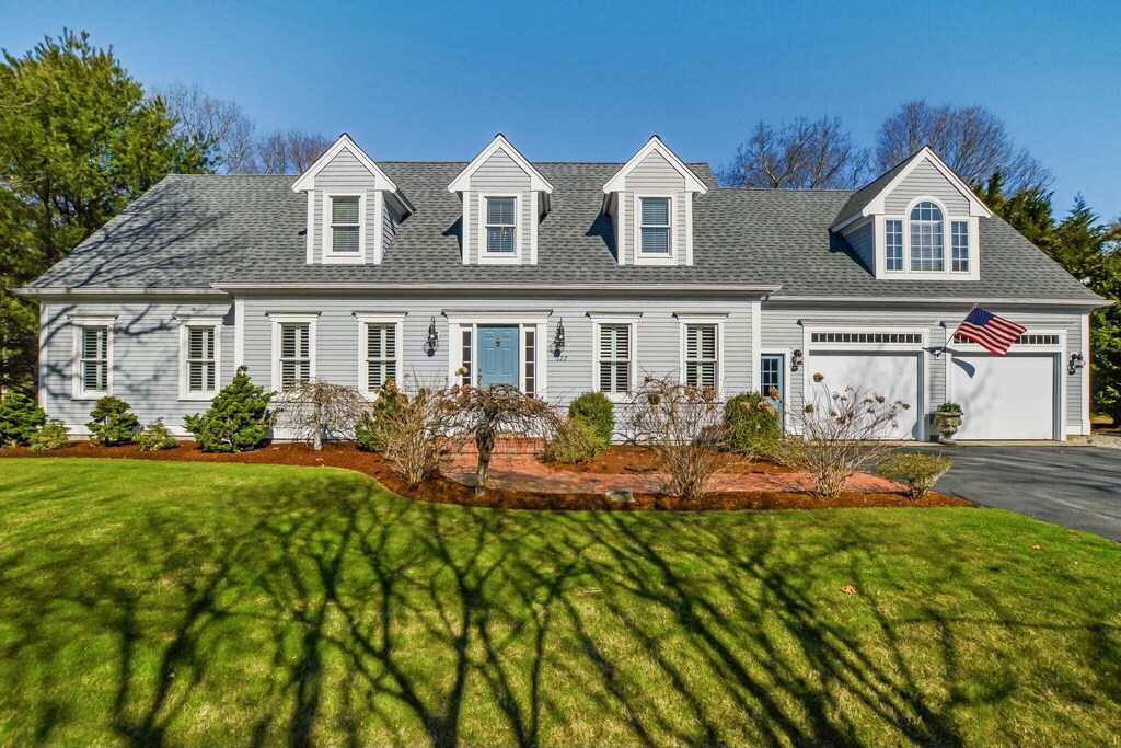 cape cod-style house featuring a front lawn, an attached garage, aphalt driveway, and roof with shingles