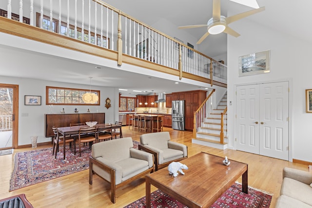 living room featuring stairs, a high ceiling, baseboards, and light wood finished floors