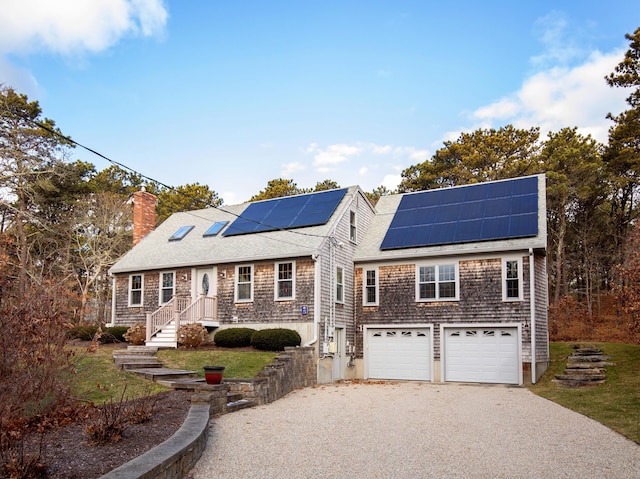 shingle-style home featuring roof with shingles, gravel driveway, solar panels, an attached garage, and a chimney