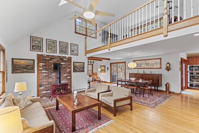 living room featuring a ceiling fan, baseboards, a high ceiling, light wood-style flooring, and a wood stove