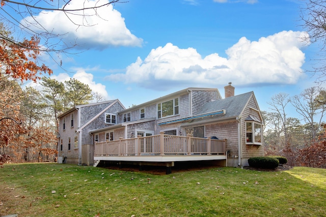 back of property with a deck, a lawn, roof with shingles, and a chimney