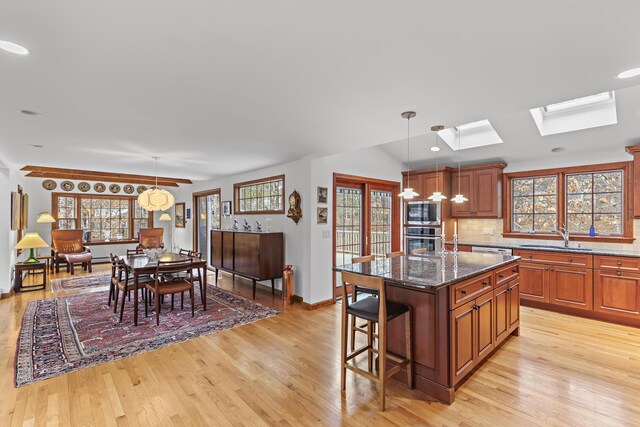 kitchen featuring backsplash, light wood-type flooring, a kitchen breakfast bar, a skylight, and stainless steel appliances