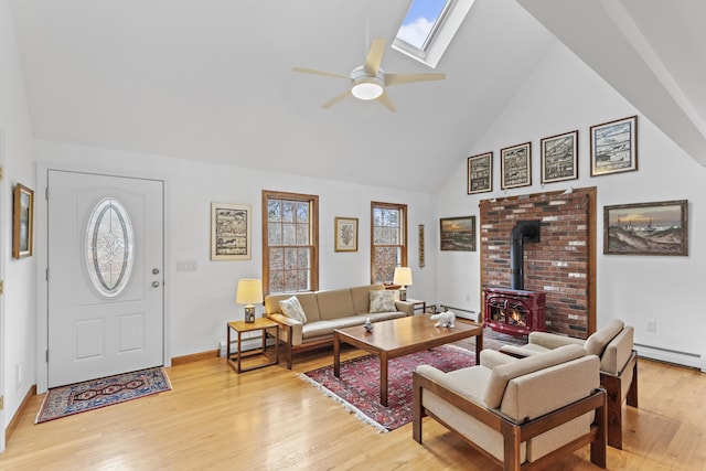 living room with ceiling fan, a skylight, a wood stove, light wood-style floors, and high vaulted ceiling