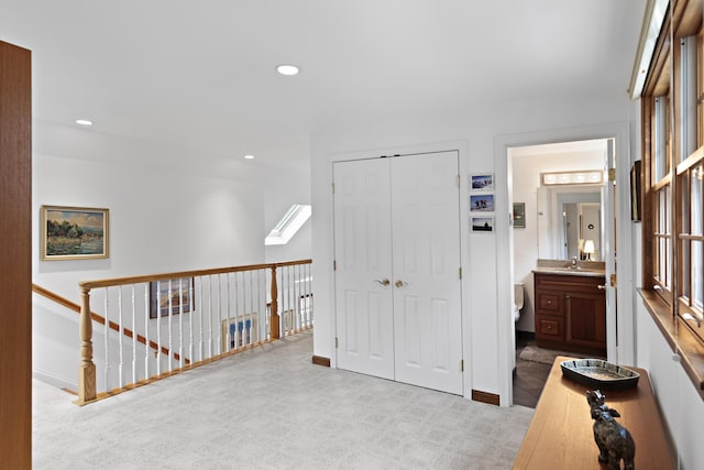 corridor featuring a sink, recessed lighting, carpet floors, a skylight, and baseboards