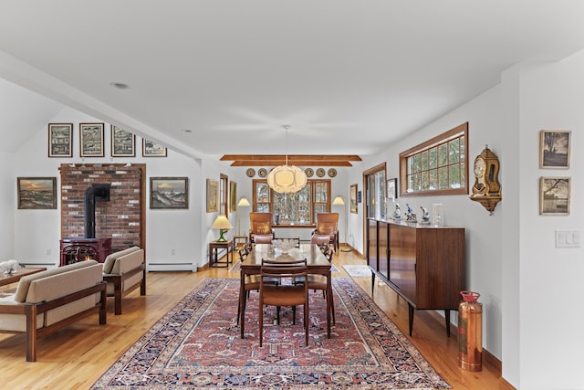 dining room featuring baseboard heating, a healthy amount of sunlight, a wood stove, and light wood finished floors