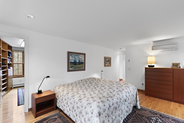 bedroom with a baseboard heating unit, light wood-style flooring, baseboards, and a wall mounted air conditioner