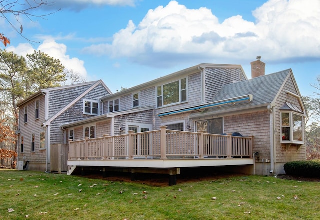 rear view of house featuring a wooden deck, a lawn, roof with shingles, and a chimney