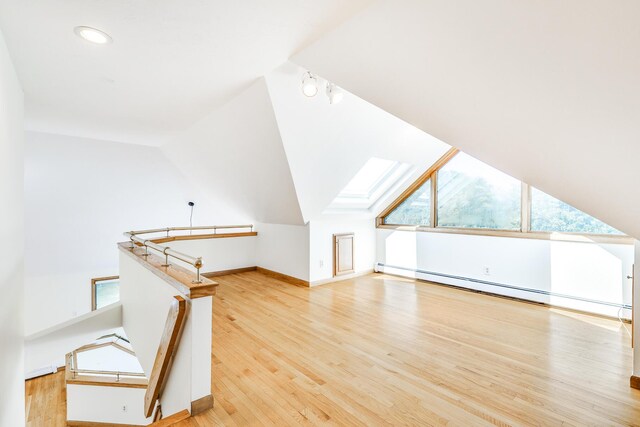 bonus room with a baseboard radiator, lofted ceiling with skylight, and light hardwood / wood-style floors