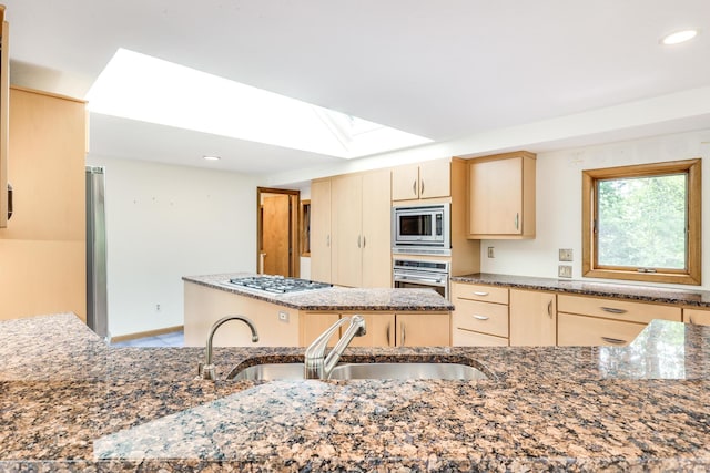 kitchen with sink, a center island, dark stone counters, light brown cabinets, and stainless steel appliances