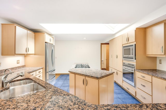 kitchen with sink, dark stone countertops, stainless steel appliances, a kitchen island, and light brown cabinets