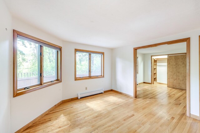 empty room featuring plenty of natural light, baseboard heating, and light hardwood / wood-style flooring