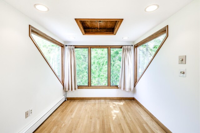 spare room featuring a raised ceiling, light hardwood / wood-style flooring, and a baseboard heating unit