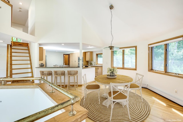 dining space featuring baseboard heating, a towering ceiling, and light hardwood / wood-style floors