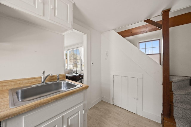 kitchen featuring a sink, light countertops, light wood-style flooring, and white cabinetry
