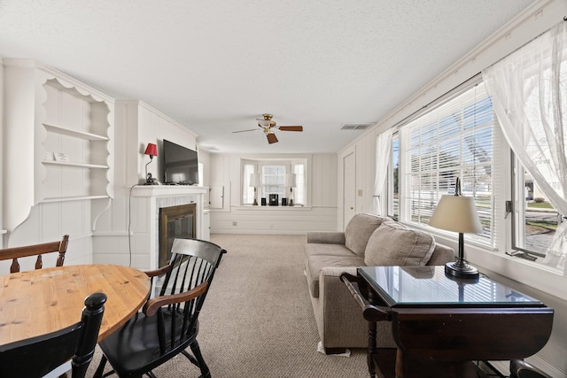 living room featuring carpet floors, a textured ceiling, a glass covered fireplace, a ceiling fan, and visible vents