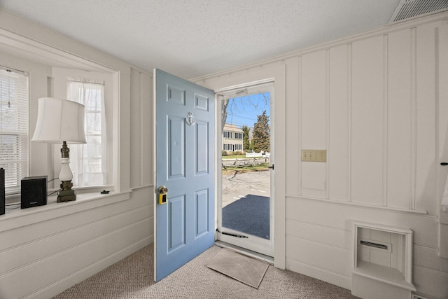 entryway featuring light colored carpet, a textured ceiling, visible vents, and a decorative wall