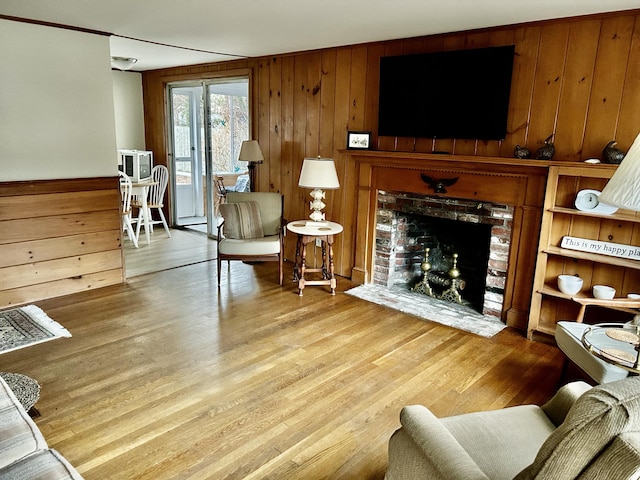 living room with a brick fireplace, light hardwood / wood-style flooring, and wooden walls