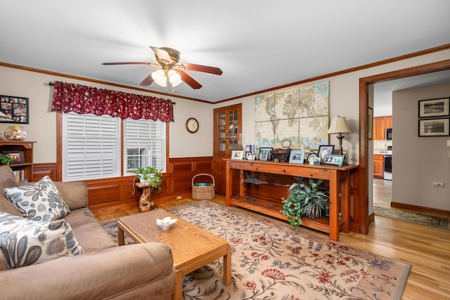 living area with ceiling fan, light wood-style flooring, a wainscoted wall, and ornamental molding