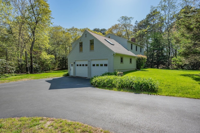 view of home's exterior with a chimney, asphalt driveway, a yard, a shingled roof, and a garage