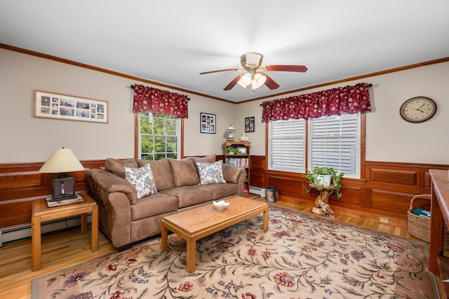 living area with healthy amount of natural light, wood finished floors, a ceiling fan, crown molding, and a wainscoted wall