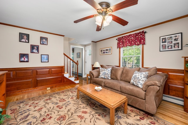 living area featuring a baseboard radiator, light wood-type flooring, ornamental molding, ceiling fan, and stairway