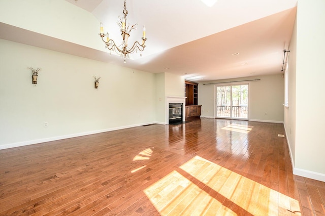 unfurnished living room with baseboards, wood-type flooring, a chandelier, and a fireplace