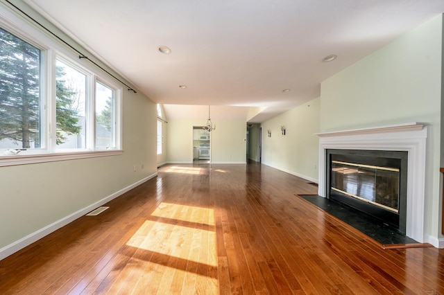 unfurnished living room featuring visible vents, baseboards, a chandelier, a fireplace with flush hearth, and hardwood / wood-style floors