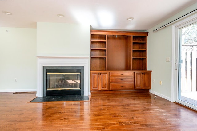 unfurnished living room with recessed lighting, a fireplace with flush hearth, wood finished floors, and baseboards