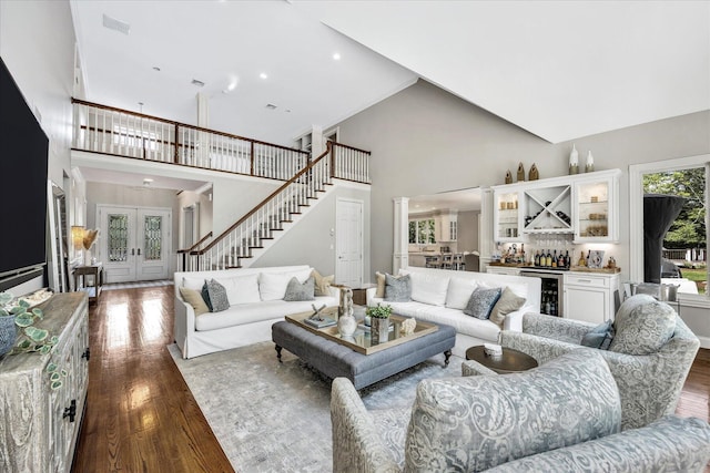living room with french doors, a bar, stairs, dark wood finished floors, and high vaulted ceiling