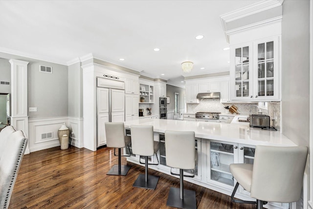 kitchen with a peninsula, under cabinet range hood, a breakfast bar area, and visible vents