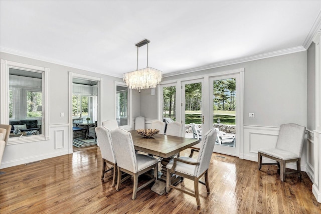 dining space with a notable chandelier, ornamental molding, visible vents, a decorative wall, and wood finished floors