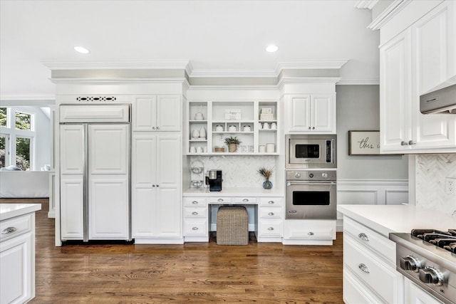 kitchen with built in appliances, light countertops, ornamental molding, and white cabinets
