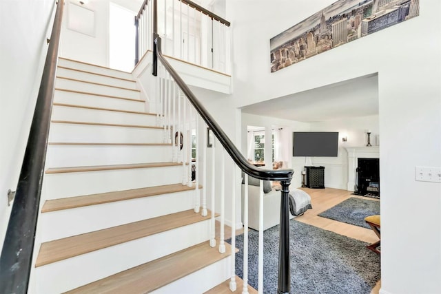 stairway featuring a fireplace with flush hearth, a high ceiling, and wood finished floors