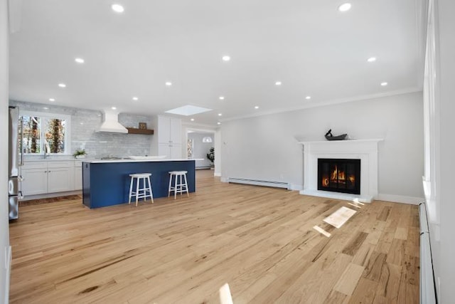 unfurnished living room featuring recessed lighting, a baseboard heating unit, light wood-style floors, and crown molding