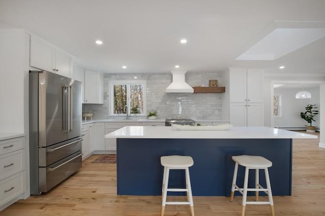 kitchen with high end fridge, a breakfast bar, a sink, white cabinets, and custom exhaust hood