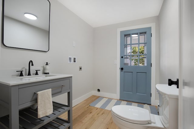 half bath with toilet, vanity, baseboards, and wood finished floors