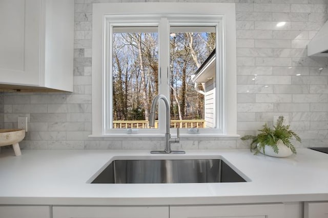 room details with backsplash, white cabinetry, light countertops, and a sink