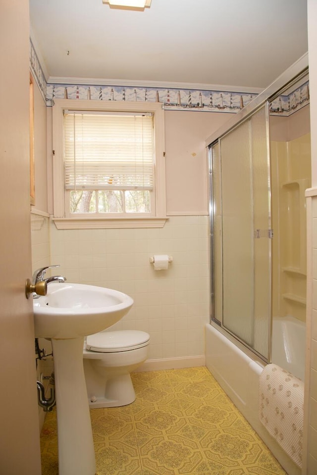 full bath featuring a wainscoted wall, tile walls, shower / bath combination with glass door, and toilet