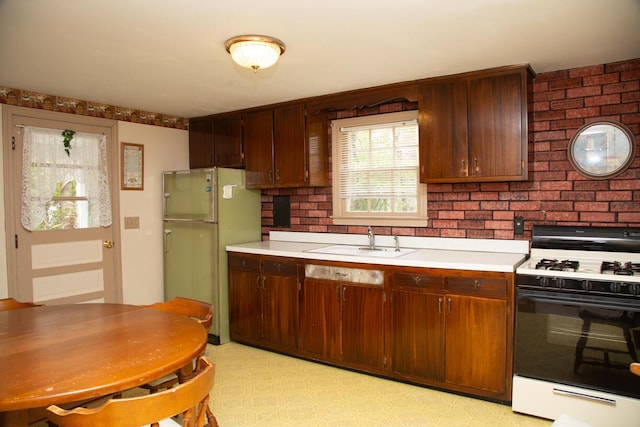 kitchen featuring a sink, freestanding refrigerator, light countertops, range with gas stovetop, and brick wall