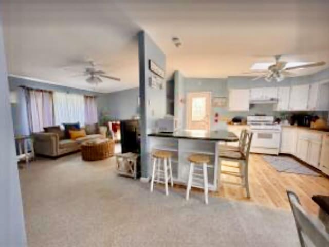 4 Coffey Ln, Dennis Port, MA 02639 - kitchen with white stove, a ceiling fan, white cabinetry, a kitchen bar, and ventilation hood