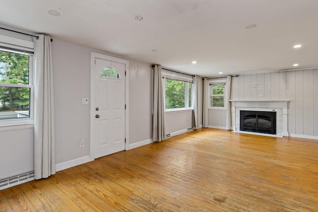 unfurnished living room with a fireplace, a baseboard radiator, light hardwood / wood-style floors, and a healthy amount of sunlight