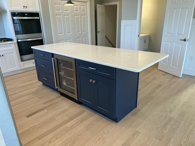 kitchen with light wood-type flooring, white cabinetry, stainless steel double oven, and wine cooler