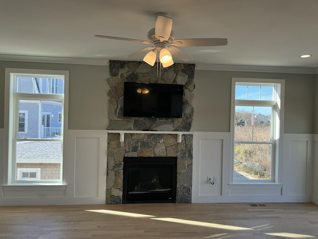 unfurnished living room with crown molding, ceiling fan, and a stone fireplace