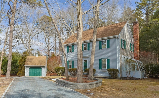 colonial inspired home featuring a garage, a shingled roof, a chimney, and an outdoor structure