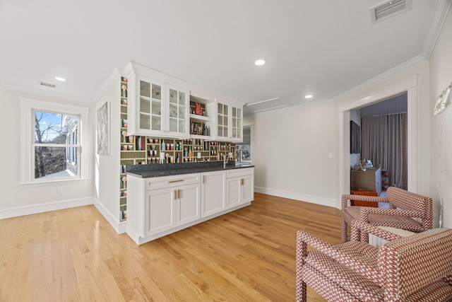 bar featuring white cabinetry, ornamental molding, decorative backsplash, dark stone counters, and light wood-type flooring