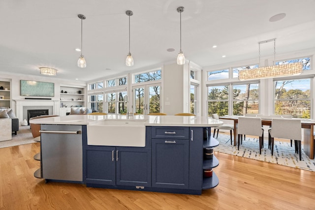 kitchen featuring an island with sink, sink, stainless steel dishwasher, and decorative light fixtures