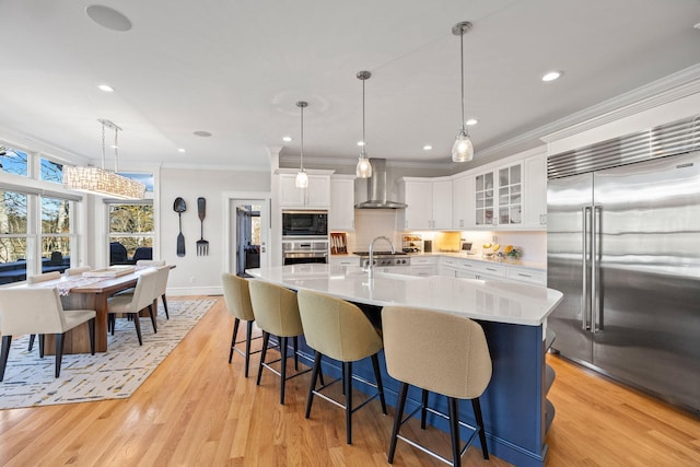 20 Chase St, West Harwich, MA 02671 - kitchen featuring built in appliances, wall chimney exhaust hood, ornamental molding, light countertops, and a breakfast bar