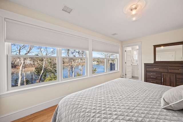 bedroom featuring a water view, ensuite bath, and light wood-type flooring